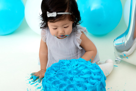 Asian baby girls first blue birthday cake smashing with balloons decoration.の写真素材