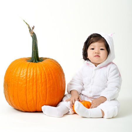 Halloween baby girl sitting with pumpkins on white backgroundの写真素材
