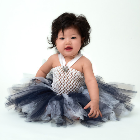 Cute Asian baby girl in flare dress sitting up.の写真素材