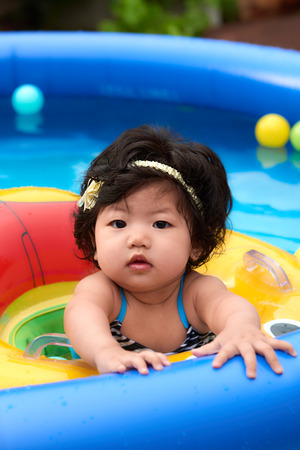 Asian baby girl in swimsuit and float swimming in pool with ballsの写真素材