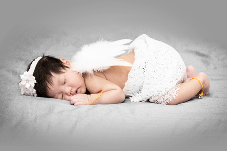 Sleeping Asian baby angel in peace. White outfit and wings.の写真素材