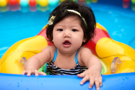 Asian baby girl in swimsuit and float swimming in pool with ballsの写真素材