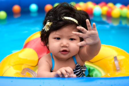 Asian baby girl in swimsuit and float swimming in pool with ballsの写真素材