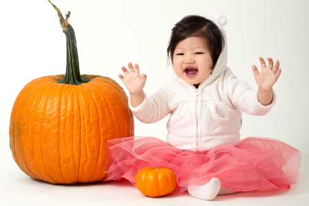 Halloween baby girl sitting with pumpkins on white backgroundの写真素材
