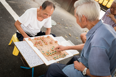 Two Chinese elderly men in 2015 playing Chinese chess outside their home in the summer as their daily routine.のeditorial素材