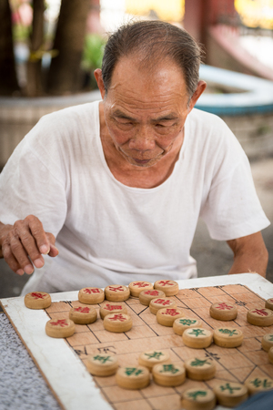 Two Chinese elderly men in 2015 playing Chinese chess outside their home in the summer as their daily routine.のeditorial素材