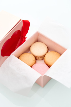 4 colorful macaroons wrapped in the Valentines Day themed pink box with red heart and bow on top of the box.の写真素材