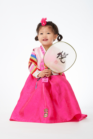 Smile Korean little girl wearing a Traditional Hanbok dress and holding a fan in white background. The characters on the dress means happiness and healthy. The character on the fan means happy.の写真素材