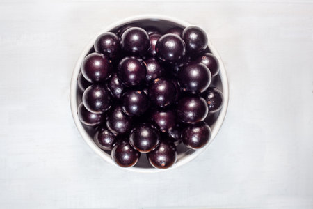 Top view of jabuticaba, an exotic tropical fruit from Brazil, arranged in a white bowl on a light...