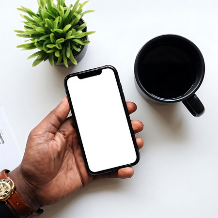 Hand holding a smartphone displaying a blank screen with document and black cup on white table. Generative AI Illustration.の素材