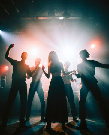 The blurry silhouettes of five teenagers are dancing happily amidst the lights of a nightclub. AI Generated.の素材
