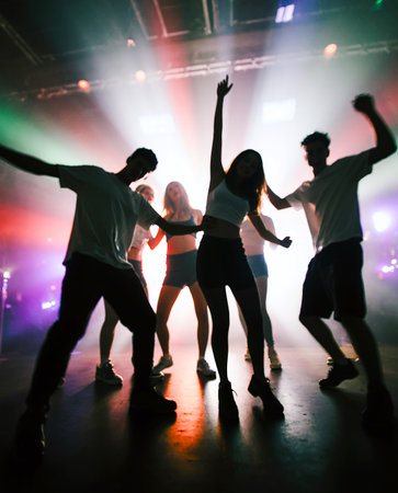The blurry silhouettes of six teenagers are dancing happily amidst the lights of a nightclub. AI Generated.の素材