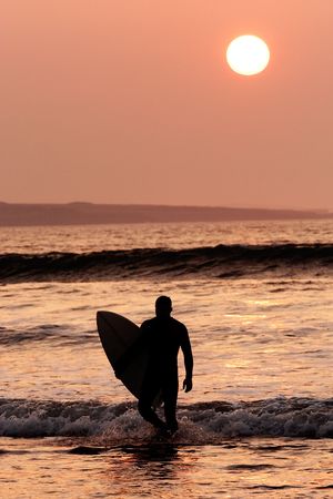 Surfer exiting the water. Silhouette of man carrying surfboardの写真素材