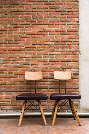 Two steel frame chairs are padded with brown cushions and a wooden backrest is placed in front of the brick wallの写真素材
