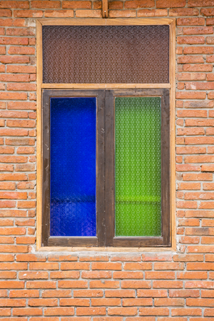 The old wooden window panes consist of blue and green glass patterns on a brick wallの写真素材