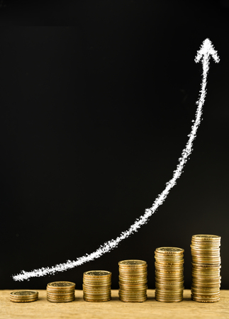 Money coin stack arranged as a graph on a wooden and write white chalk arrow indicates economic upturn on blackboard, concept of money growthの写真素材