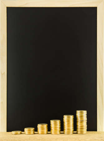 Money coin stack arranged as a graph on a wooden with blank blackboard backgroundの写真素材