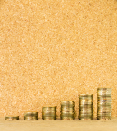 Money coin stack arranged as a graph on a wooden with blank cork board background, concept of money...