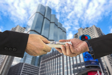 Businessman hand receiving stack of dollar bills money to another hand with blurred office backgroundの写真素材