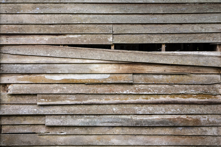 The old wooden wall house is ruined and one piece of old wood is falling down with can see the inner darkness as texture and backgroundの写真素材