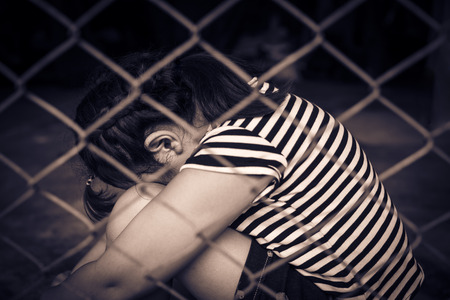 The sad girl child hug her knee, while sitting alone in cage was imprisoned make no freedom or lack...