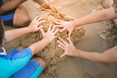 The girl child and parents are using their hands to pile sand on the beach, which is a time to relax in the summerの写真素材