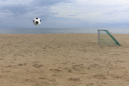 Soccer ball flying through the air above on sand beach field and entering the goalの写真素材