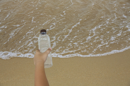Girl child hands holding empty bottles to dispose into the beach, concept of create environmental pollutionの写真素材
