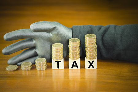 Coins stack on top of word tax on wooden block with thieves wear black gloves, concept of tax evasion avoidanceの写真素材