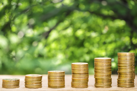 Money coins arranged as a graph on wooden table with natural bokeh background, concept of business growth and saving moneyの写真素材