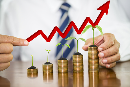 Tree growing and soil on money coin stack arranged as a graph on wooden table with businessman hand holding red arrow over, concept of money growth and saving moneyの写真素材