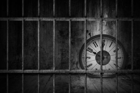 Distorted soft melting clock is imprisoned in old prison rusted metal bars with dark and dim light, concept of losing valuable time and trap in businessの写真素材