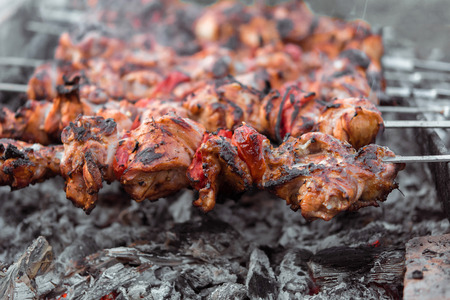 Close up shot of appetizing hot shish kebab with tomatoes on metal skewers prepares on the coals outdoors. Grilling shashlik on barbecue grill.の写真素材