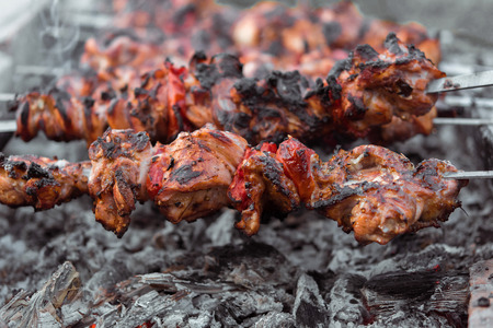 Close up shot of appetizing hot shish kebab with tomatoes on metal skewers prepares on the coals outdoors. Grilling shashlik on barbecue grill.の写真素材