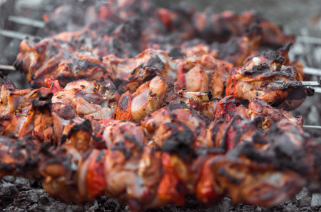 Close up shot of appetizing hot shish kebab with tomatoes on metal skewers prepares on the coals outdoors. Grilling shashlik on barbecue grill.の写真素材