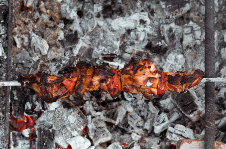 Close up shot of appetizing hot shish kebab with tomatoes on metal skewers prepares on the coals outdoors. Grilling shashlik on barbecue grill.の写真素材