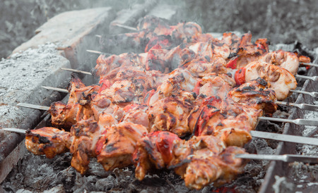 Close up shot of appetizing hot shish kebab with tomatoes on metal skewers prepares on the coals outdoors. Grilling shashlik on barbecue grill.の写真素材