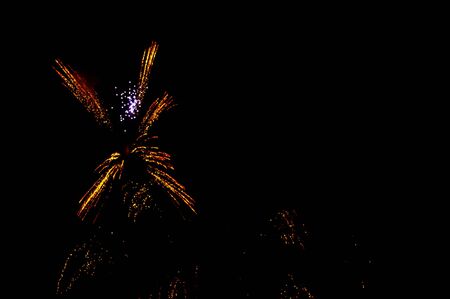 Yellow and red fireworks in the shape flower on the left side on a black background.