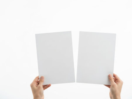 The image depicts a pair of hands holding two pieces of torn white paper against a plain white background. The hands are positioned in such a way that the torn edges of the paper are clearly visible, creating a minimalist and stark visual effect. The simplicity of the image emphasizes the contrast between the white paper and the background, highlighting the texture and roughness of the torn edges. The overall composition is clean and uncluttered, focusing solely on the interaction between the hands and the paper.の素材