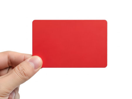 The image depicts a hand holding a bright red identification card against a plain white background. The card appears to be rectangular and has a smooth, glossy finish. The hand is positioned such that the thumb and index finger are holding the card from the sides, while the other fingers are slightly curled. The image focuses on the card and the hand, with no other objects or text present.の素材