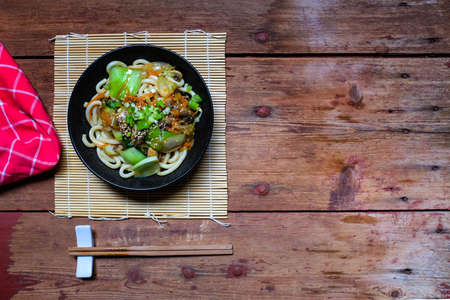 Healthy Japanese dish; Vegetarian Udon Yaki. Udon stir fried with Bok choy, carrot, onion and champignons in garlic, ginger and soy sauce. On wooden table with copy space.の写真素材