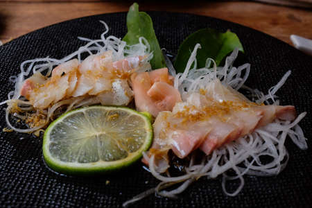 Sea Bream sashimi marinated with ginger, lemon, mirin, wasabi and soy sauce. Garnished by radish and lime leaf.の写真素材