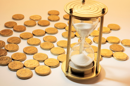 Hourglass and Coins on Warm Backgroundの写真素材