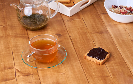 Tea in glass cup on the wooden table and toast with plum jam.の写真素材