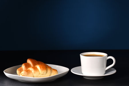 Croissant and coffee in white dishes on dark background.の写真素材