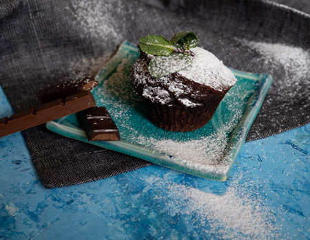 Delicious chocolate muffin with powdered sugar and mint sprig on light blue textured backgroundの写真素材