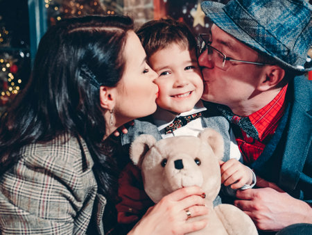 Happy new year and christmas. Loving parents kiss on both sides of their little son. Cheerful and joyful family in beautiful New Years decorations.の写真素材