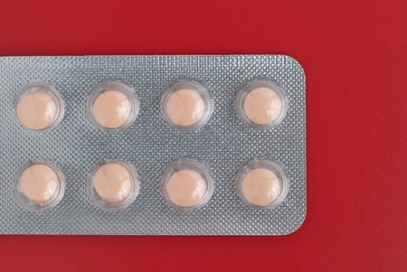 Close-up of a pack of orange pills on red background.