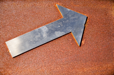 Aluminium arrow, pointing up, on rusty backgroundの写真素材
