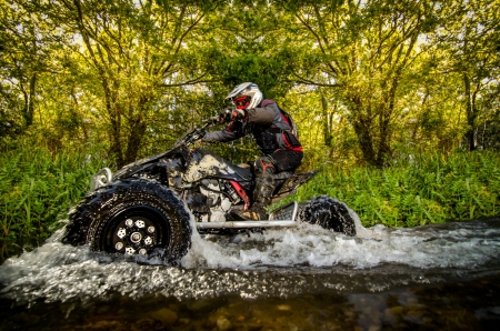 Quad rider through water stream in the forest.の写真素材